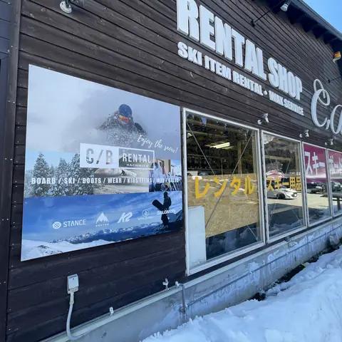 RENTAL SHOPの立体文字が付いた木造の店舗外観。左の壁に青い写真看板を掲出